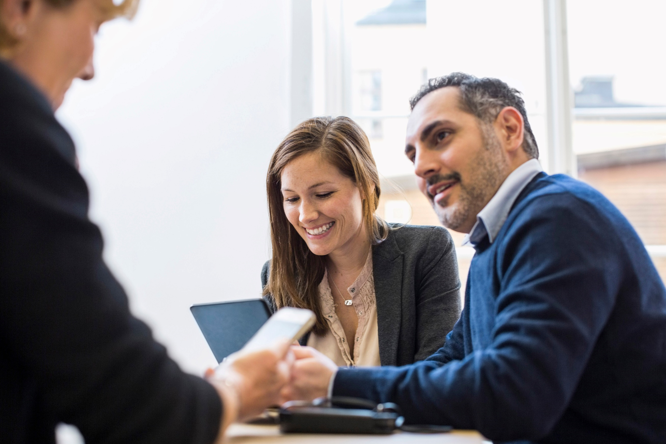 Three people having a meeting in an office; one woman is on her laptop